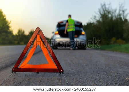 Broken silver luxury car emergency accident. Man driver installing red triangle stop sign on road. Sport automobile turned on blinkers technical problems on the road. Safety procedure vehicle broken Royalty-Free Stock Photo #2400155287