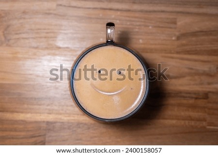 Good morning coffee smile cup on wooden background. Cup of delicious hot coffee with foam and smile on color background, top view. Happy morning, good mood, inspiration Royalty-Free Stock Photo #2400158057