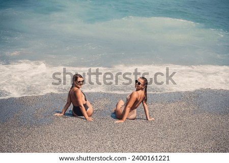 Two girls girlfriend are sitting on the sea sandy shore and the waves soaked them in bathing suits on a sunny warm day