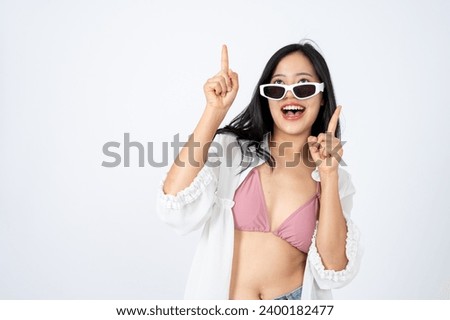 Young elegant Asian woman in summer clothes and sunglasses is pointing her finger at an empty copy space on isolated white background. summer vacation, beach holiday, traveller