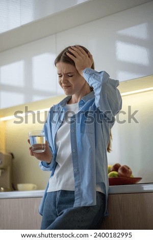 Tired exhausted woman feeling headache holding head with closed eyes on kitchen at home. Stressed girl suffers pain, migraine, cephalalgia, premenstrual syndrome taking medications, painkillers Royalty-Free Stock Photo #2400182995