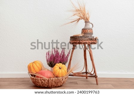 Autumn still life with pumpkins, wheat ears and heather flowers in wicker basket near white wall