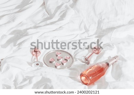 Pink champagne glasses with metal shiny, bottle of rose sparkling wine ,pink candle hearts on bed. Natural daylight, star filter effect. Valentine's Day holiday, love concept, romance evening, above