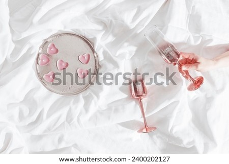 Top view Pink shining champagne glass in female hand, candles as hearts on bed cloth. Lifestyle aesthetic photo, star filter effect. Valentine's Day, love concept, romance mood. Sparkling wine.