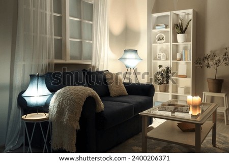 Interior of modern living room with black sofa, coffee table and glowing lamps at evening Royalty-Free Stock Photo #2400206371