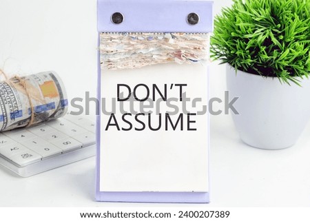 DO NOT ASSUME text, word, inscription on a desktop calendar on a white background next to money and a green flower