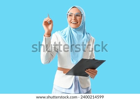 Young Muslim businesswoman with clipboard on blue background