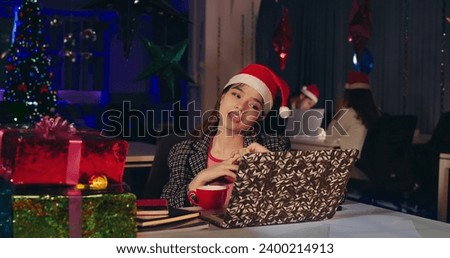 Indian smiling young woman in santa hat sitting on chair use laptop enjoy night Christmas celebrate party indoor office. Happy beautiful teenager girl making online distant gossips video call