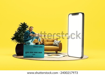 Emotional man sitting on credit card and pulling robe from giant 3D model of mobile phone with empty screen over light background. Online shopping, sales, e-payment. Mockup for text, ad, design, logo