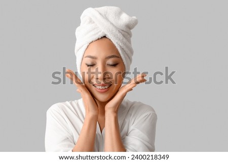 Young Asian woman in gown after shower on light background, closeup Royalty-Free Stock Photo #2400218349