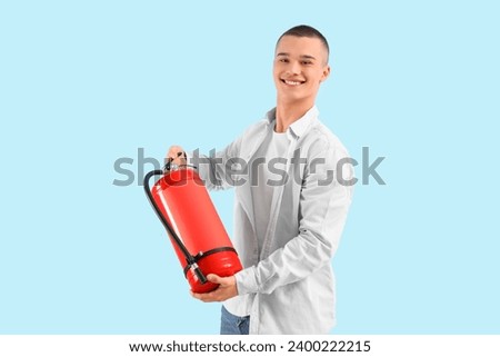 Teenage boy with fire extinguisher on blue background Royalty-Free Stock Photo #2400222215