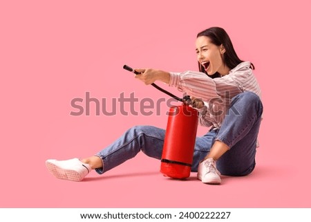 Scared young woman with fire extinguisher on pink background