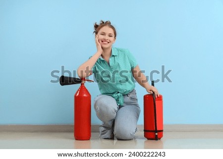 Young woman with fire extinguishers near blue wall