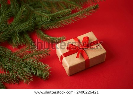 The gift is wrapped in craft paper and wrapped with a red ribbon on a red background. The concept of the New Year holidays.