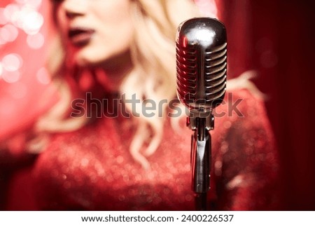 Close up drag queen performer with retro microphone singing on stage in spotlight, copy space Royalty-Free Stock Photo #2400226537