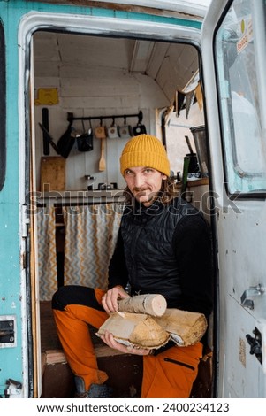 A guy holds a bundle of firewood in his hands to light a fireplace, a hiker stocks up on logs, spending the night in the wild in a campsite in winter. High quality photo