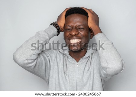 Happy cheerful young African gen Z isolated on white background. Funny smile teen student with hands on head in agonizing pain