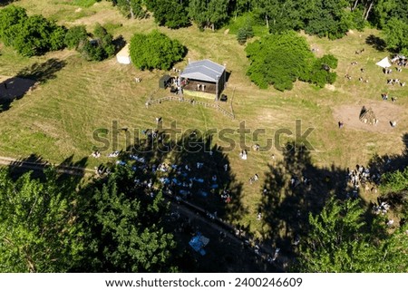 Aerial view of a summer festival in nature with a stage and people hiding in the shade of trees from the sultry sun Royalty-Free Stock Photo #2400246609