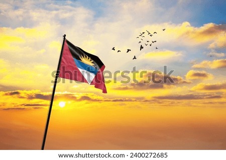 Waving flag of Antigua and Barbuda against the background of a sunset or sunrise. Antigua and Barbuda flag for Independence Day.