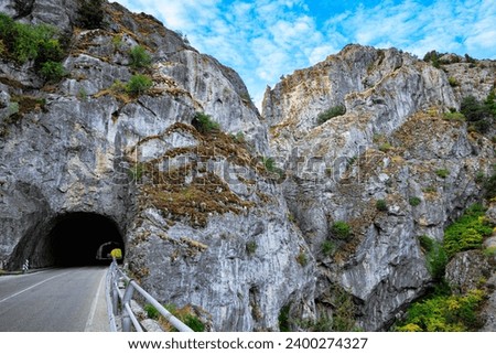 The asphalt highway passes among steep rocks and disappears into a tunnel. Gray rocks illuminated by sunset. The trip to Spain. 