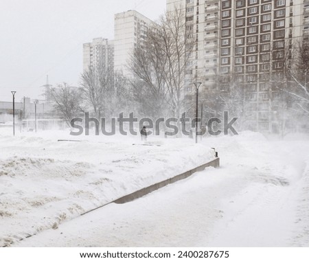 A lonely silhouette of a man walking through a snowstorm along a city street on a winter day. Snowfall, blizzard and wind in December in Moscow. Royalty-Free Stock Photo #2400287675