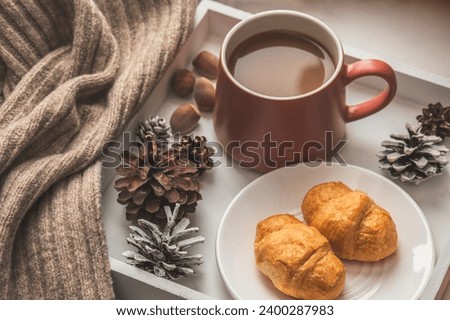 White tray with coffee and croissants and a knitted scarf on the windowsill. Cozy winter composition.