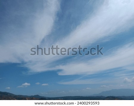 This is a photo of a beautiful blue sky with white clouds and mountains in the background