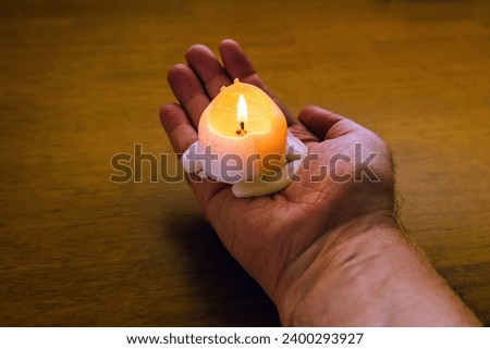 Burning candle on the palm.Man holding lighted wax candle on a wooden background.Male holding a candle in the dark.