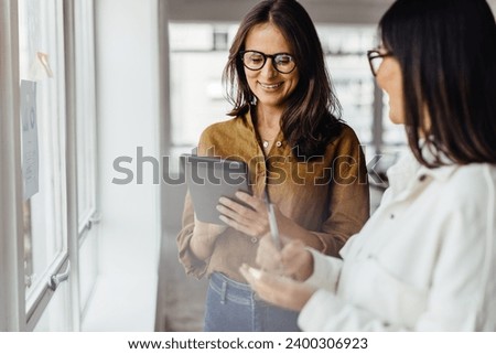 Business women standing next to a window and discussing their ideas. Female business professionals brainstorming using stocky notes and a tablet. Royalty-Free Stock Photo #2400306923