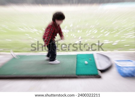 Exterior photo view of a young kid child boy golfer playing golf sport with a speed fast dynamic motion effect when he does his swing to kick the golf ball on a outdoor practice court

