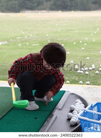 Exterior photo view of a young kid child boy golfer playing golf sport by outting his golf ball right on the Tee to kick the golf ball on a outdoor practice court