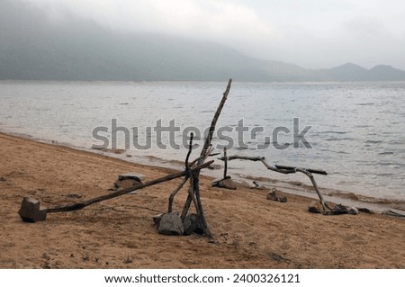Exterior photo view of a beach sand with a camp site base made fro wood sticks and branches near a lake sea ocean in an outdoor wild location with  nothing around