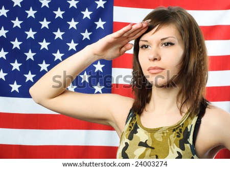beautiful young woman standing opposite an American flag and wearing camouflage salutes
