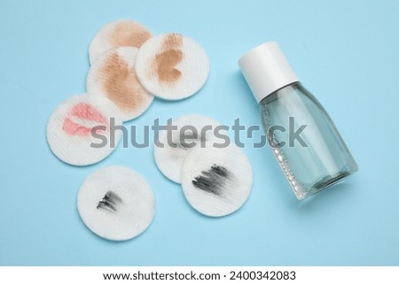 Bottle of makeup remover and dirty cotton pads on light blue background, flat lay