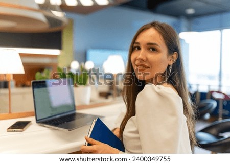 Young woman employee smiles during photosession at coworking premise. Employee enjoys photoshoot at shared workspace during break Royalty-Free Stock Photo #2400349755