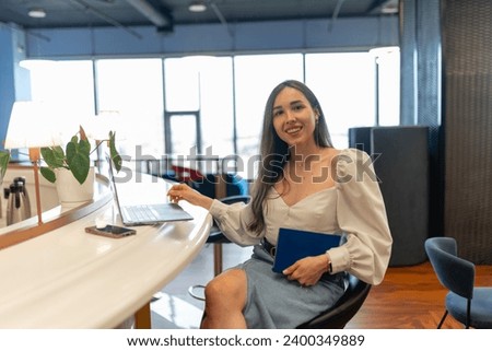 Young woman employee wears wide-sleeved blouse and laughs during photosession. Coworker smiles and laughs during photoshoot at coworking premise Royalty-Free Stock Photo #2400349889