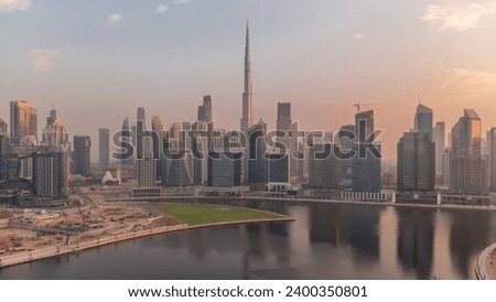 Aerial view to Dubai Business Bay and Downtown during sunrise with the various skyscrapers and towers along waterfront on canal timelapse. Construction site with cranes. Sun reflected from glass