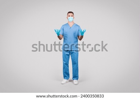 Professional male surgeon in blue scrubs stands ready with protective gloves and a face mask, showcasing preparedness and safety in medical care