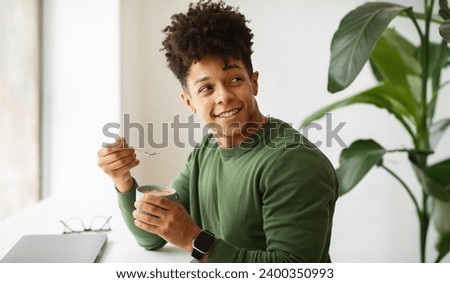 Handsome stylish young black guy freelancer have coffee break while working at cafe, sitting at table with laptop computer on, holding cup with hot chocolate, looking at copy space, panorama