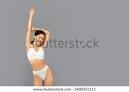 Joyful asian millennial woman in white underwear smiling and closing eyes, enjoy spare time, body care, isolated on grey studio background. Happiness and physical wellbeing Royalty-Free Stock Photo #2400351111