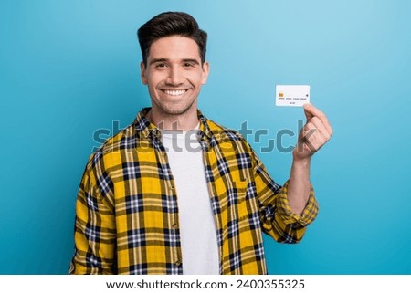 Photo of cheerful positive pleasant man with bristle dressed plaid shirt holding credit card in fingers isolated on blue color background