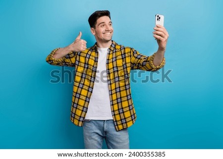 Photo of charming confident guy wear yellow checkered shirt showing thumb up tacking selfie modern device isolated blue color background