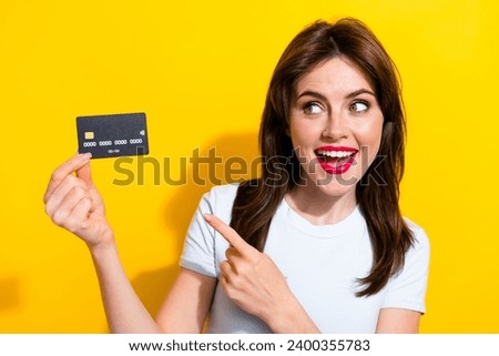 Photo of excited pretty woman with brunette hair dressed white t-shirt look directing at debit card isolated on yellow color background