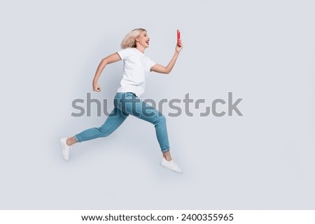 Full size photo of cheerful woman dressed white t-shirt denim pants fast run look at smartphone isolated on white color background