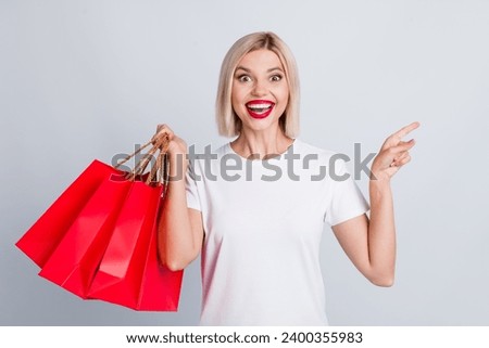 Portrait of impressed girl wear t-shirt hold new clothes indicating at unbelievable sale empty space isolated on gray color background