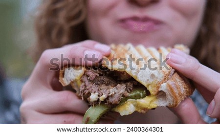 Young woman with curly hair bites and eats an appetizing delicio Royalty-Free Stock Photo #2400364301