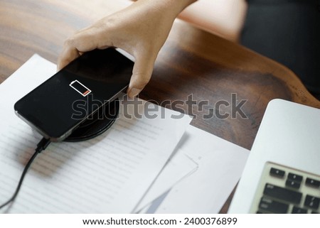 Charging mobile phone battery with wireless charging device in the table. Smartphone charging on a charging pad. Mobile phone near wireless charger Modern lifestyle technology concept.