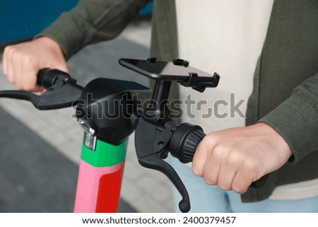 Man riding electric kick scooter with smartphone outdoors, closeup
