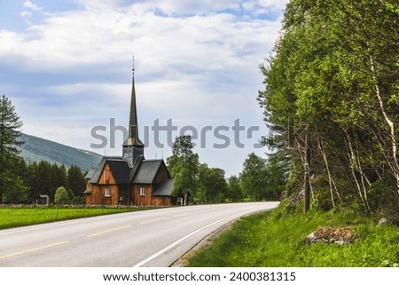 A scenic road winds towards the ancient Kvikne kirke in Innlandet, Norway, a wooden church with a tall spire, gracefully encircled by green trees, depicting a serene and historic tableau Royalty-Free Stock Photo #2400381315