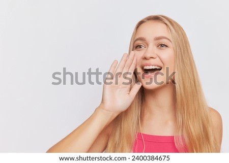 Young pretty woman with long blond hair posing with hand near her mouth over studio background, young people concept, copy space.